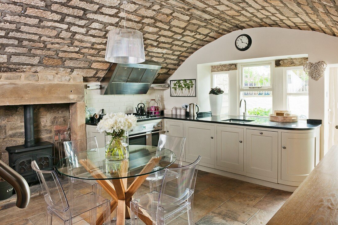 Rustic vaulted ceiling, designer furniture and traditional log burner in elegant country-house kitchen