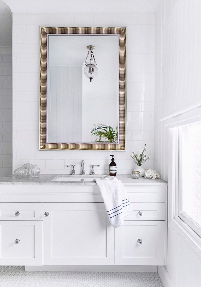 White vanity with marble top and wall mirror on tiled wall