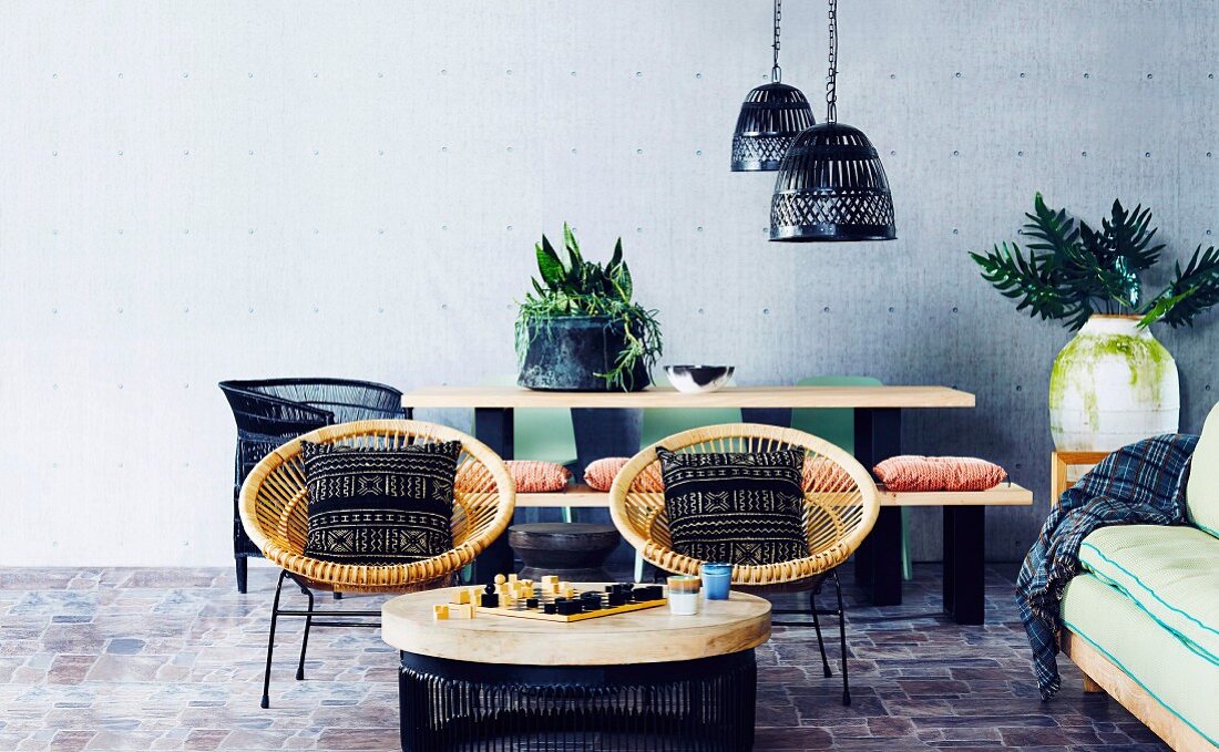 Two wicker armchairs with cushions, coffee table with board game and black lampshades over dining table