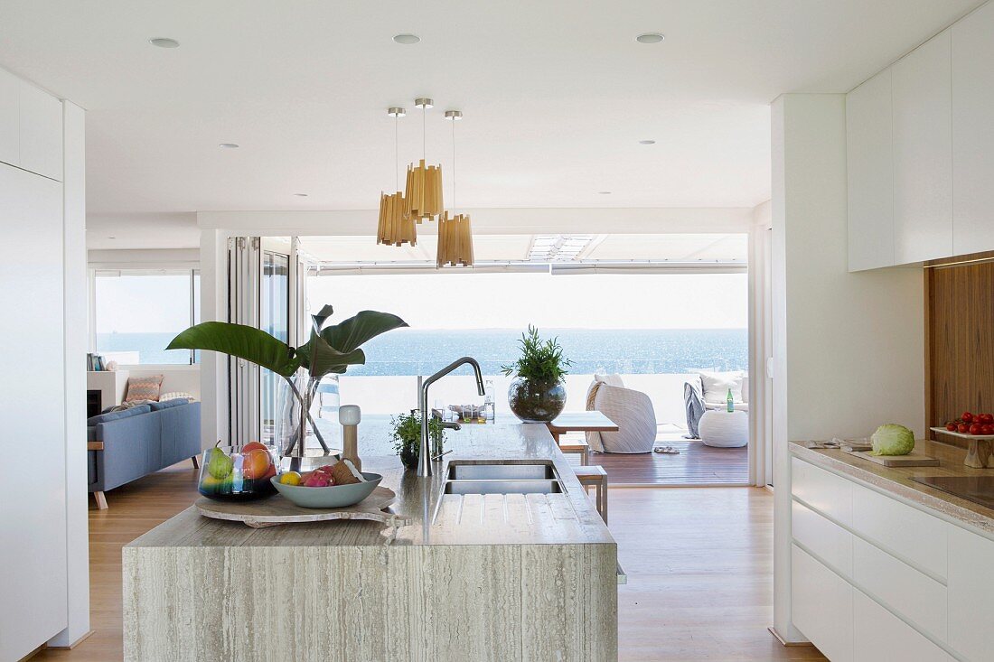 Blick von offener Desingerküche durch geöffnete Fensterfront auf Terrasse und Meer