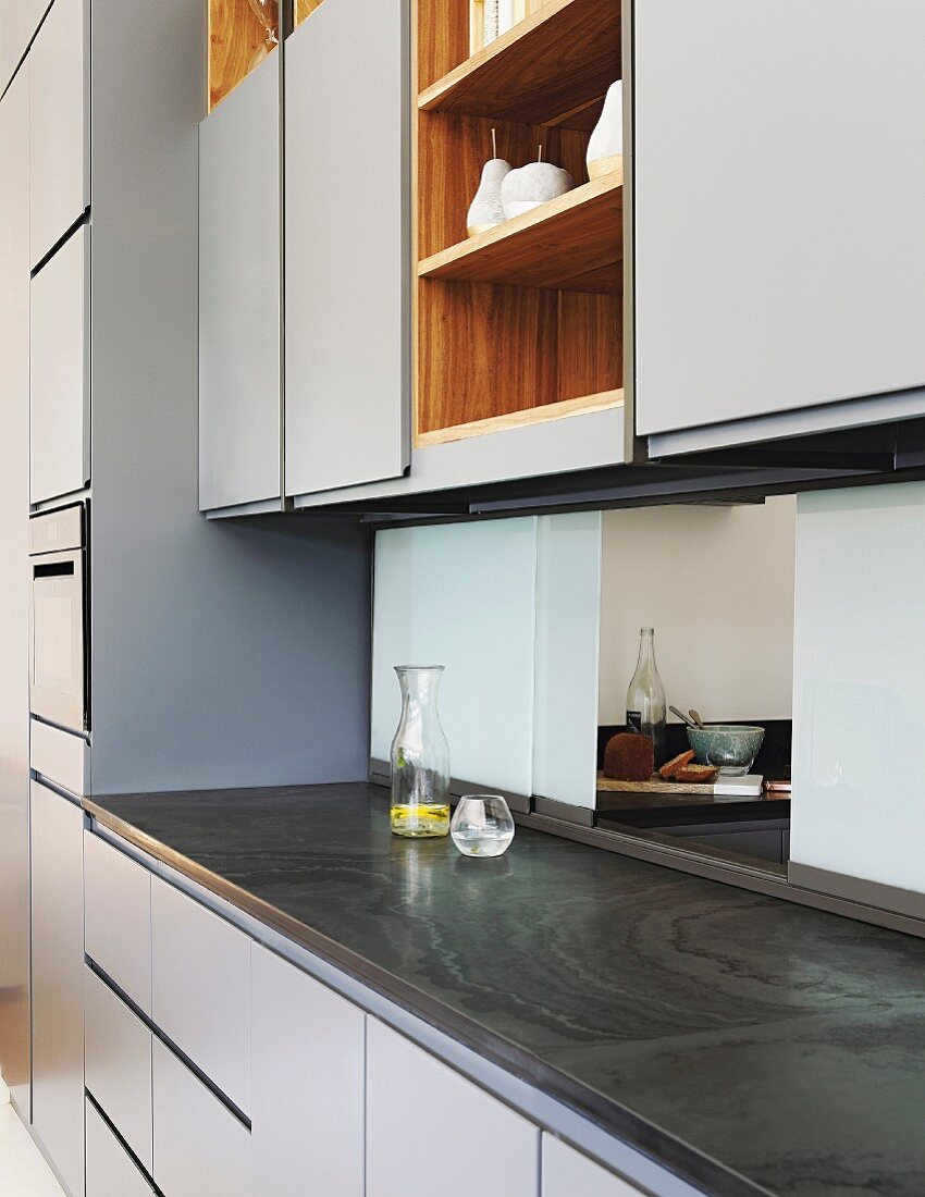 Elegante, graublaue Einbauküche mit Durchreiche aus Glasscheiben