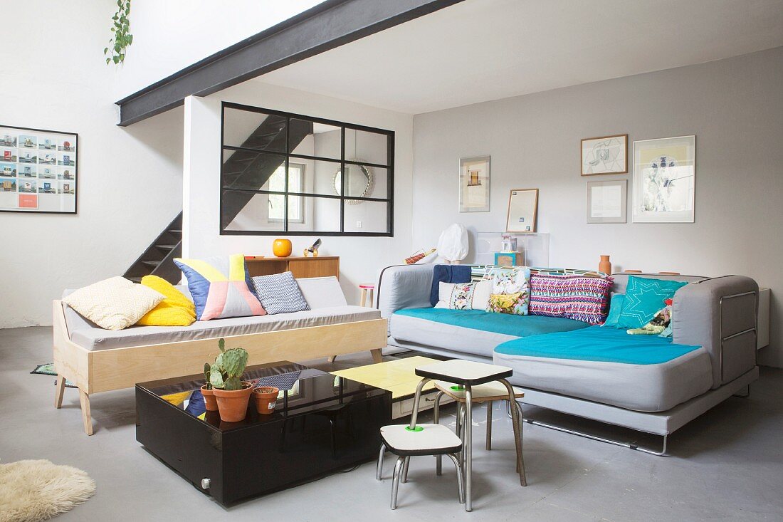 Colourful scatter cushions on sofa and black stairs leading to mezzanine