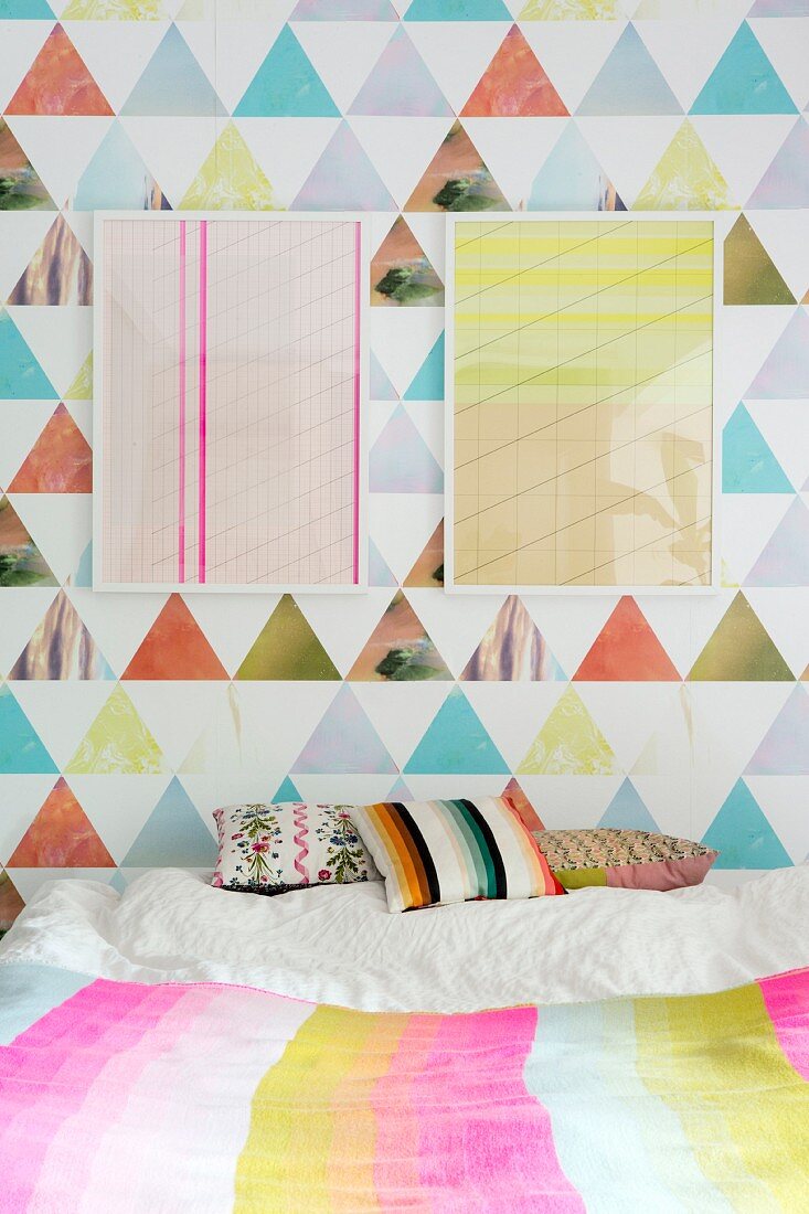 Zwei grafische, gerahmtes Bilder an bunter Tapete über Bett mit Dekokissen