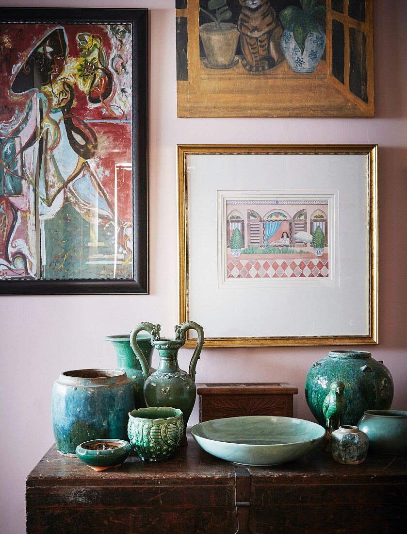 Türkisfarbene Keramikgefäße auf Vintage Holztruhe und Ethno-Bilder an pastellfarbener Wand