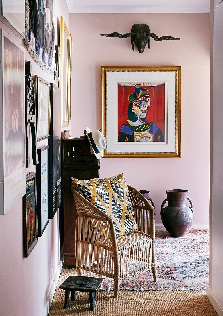 Eingangsbereich mit Korbsessel und Schemel vor Bildergalerie an rosa Wand