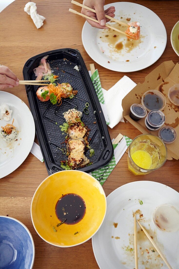 Tisch mit Sushi und Hände mit Essstäbchen