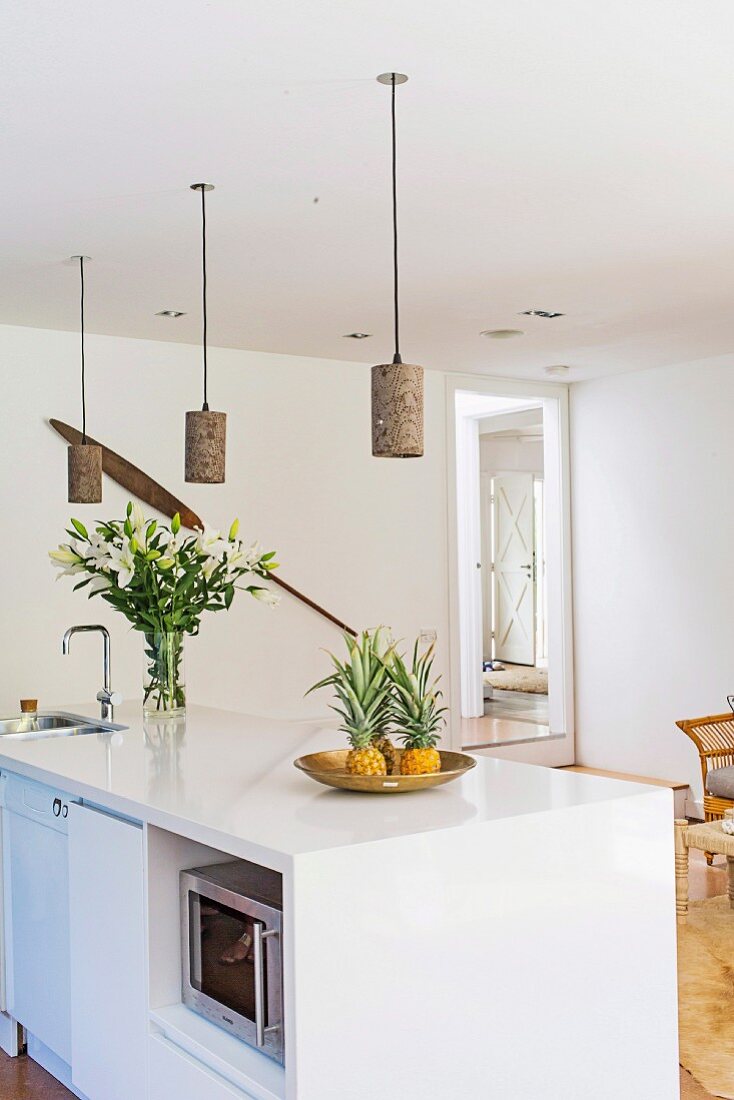 weiße Kücheninsel mit Ananas und Lilienstrauss, darüber DIY-Pendelleuchten aus Windlichtern