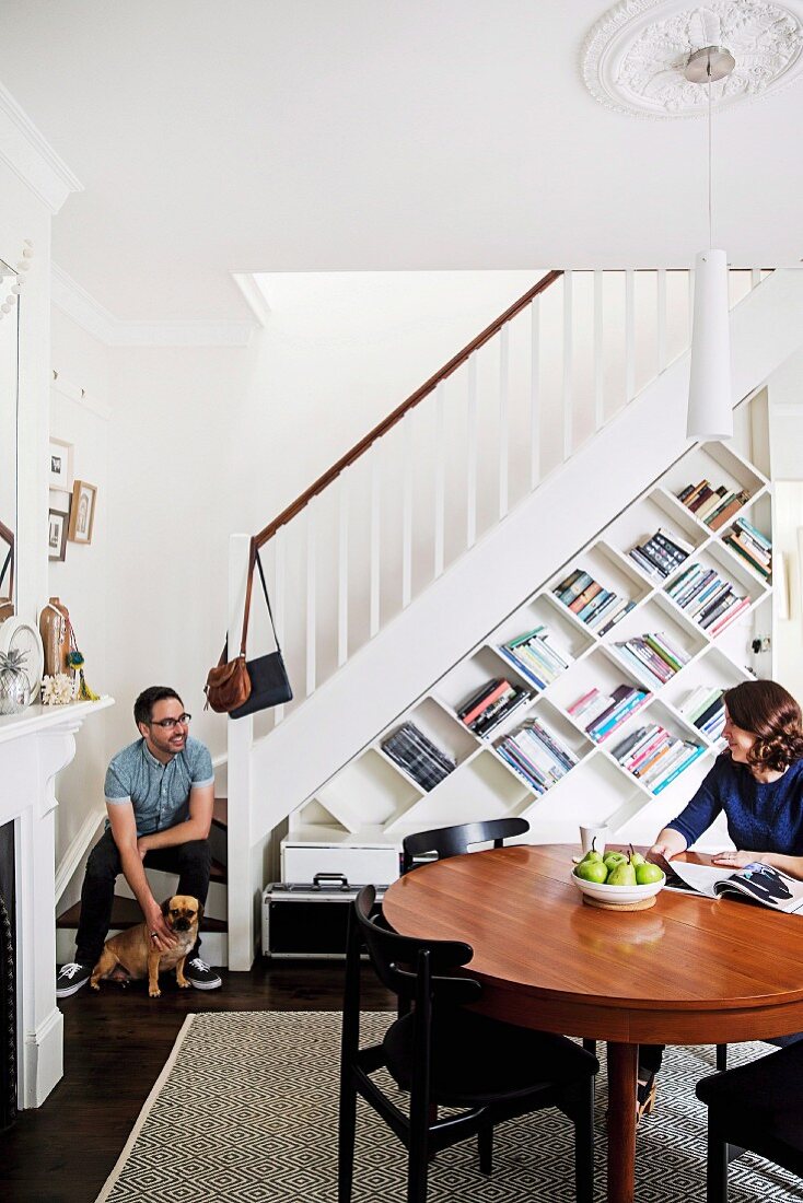 Couple with dog in dining room with bookcase under stairs