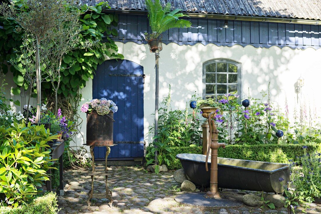 Nostalgische Gartendekoration mit Brunnen und Zinkbadewanne vor Landhaus