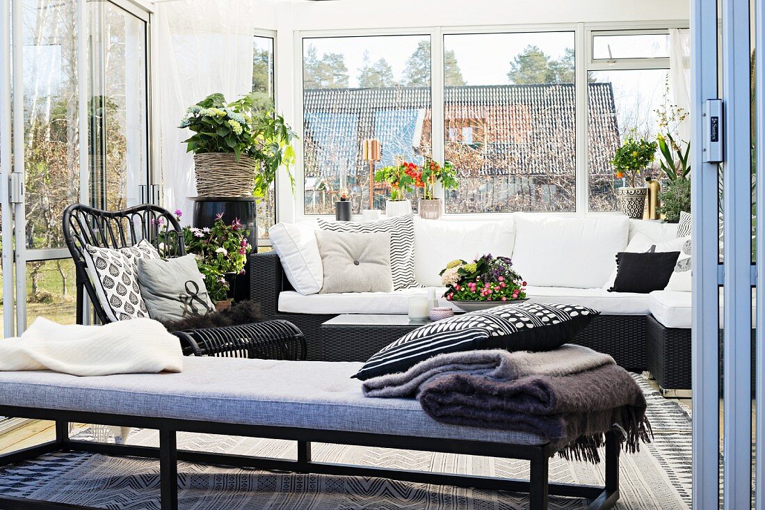 Tagesliege vor gemütlicher Couch mit weissen Polstern in Wintergartenanbau mit Zimmerpflanzen