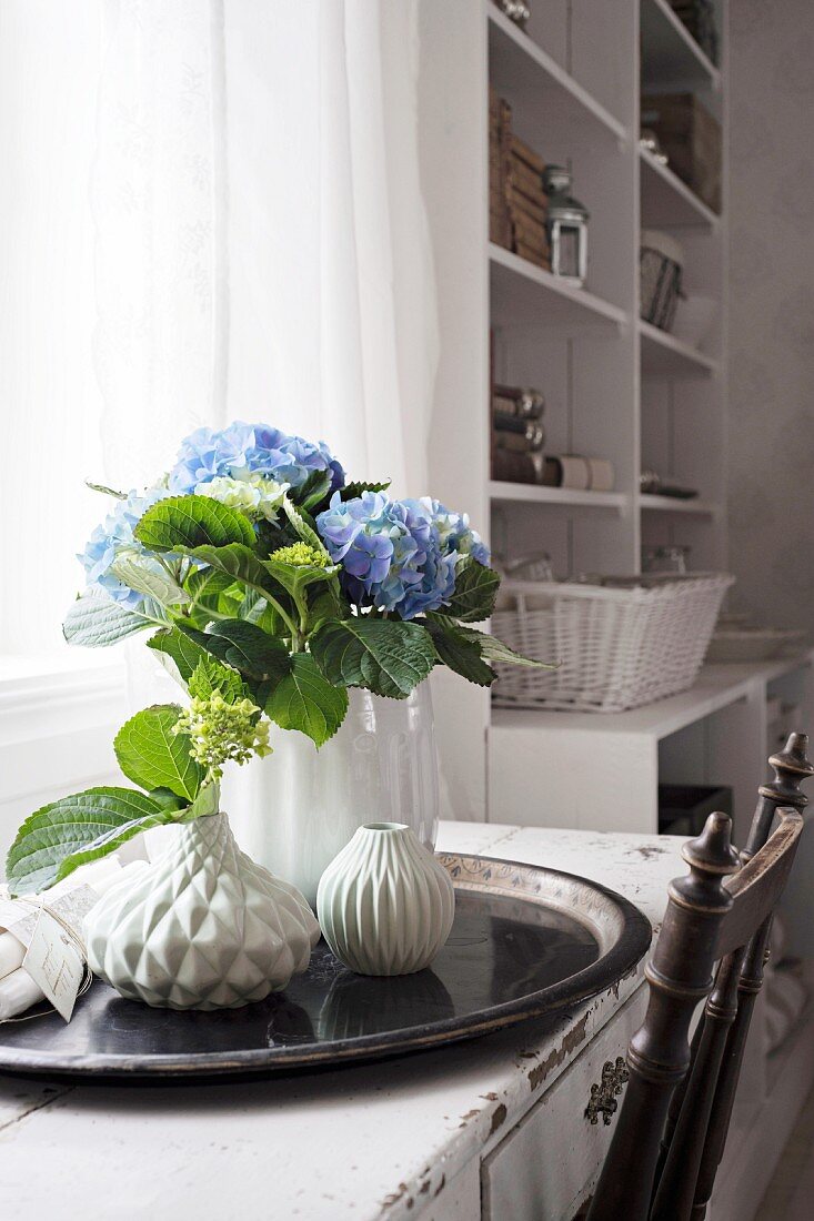 Blue hydrangea and structured vases on black tray