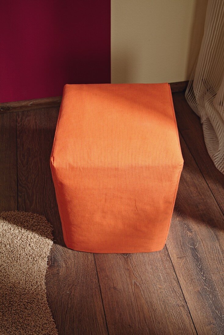 Selbstgebauter Sitzhocker aus Karton mit orangenem Bezug