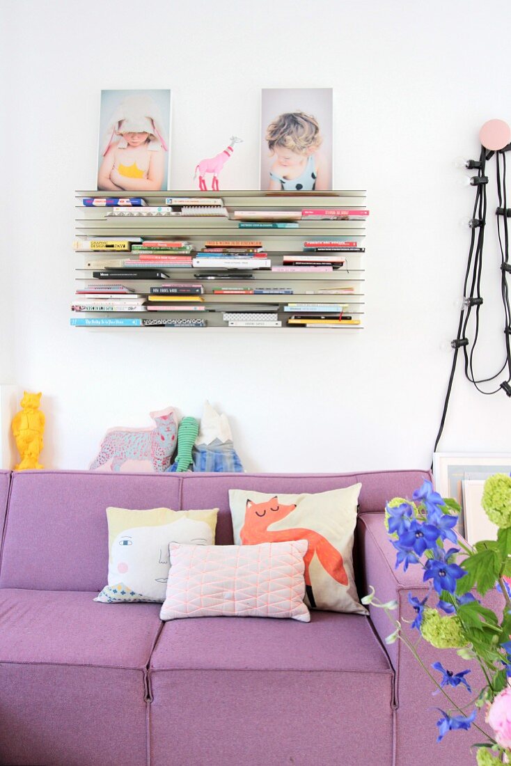 Scatter cushions on lilac couch below bookshelves