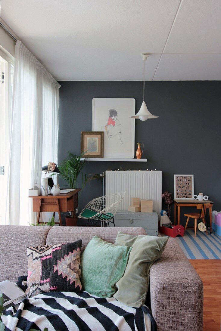 Blick über Couch auf Retro Schreibtisch und Kinderspielecke vor grauer Wand