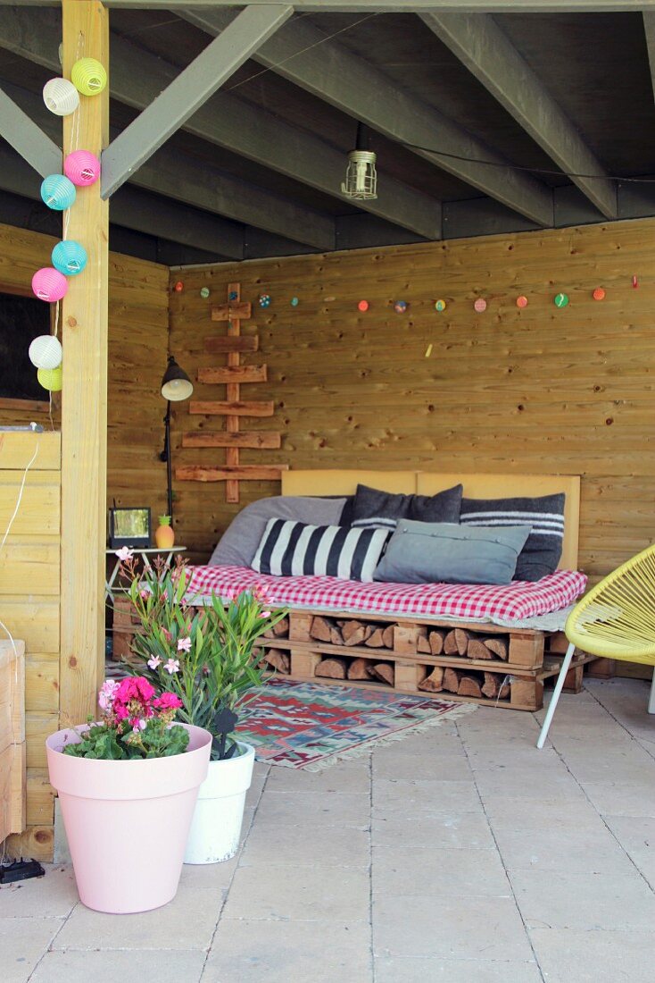 DIY pallet couch, cushions and colourful fairy lights on cosy, roofed terrace