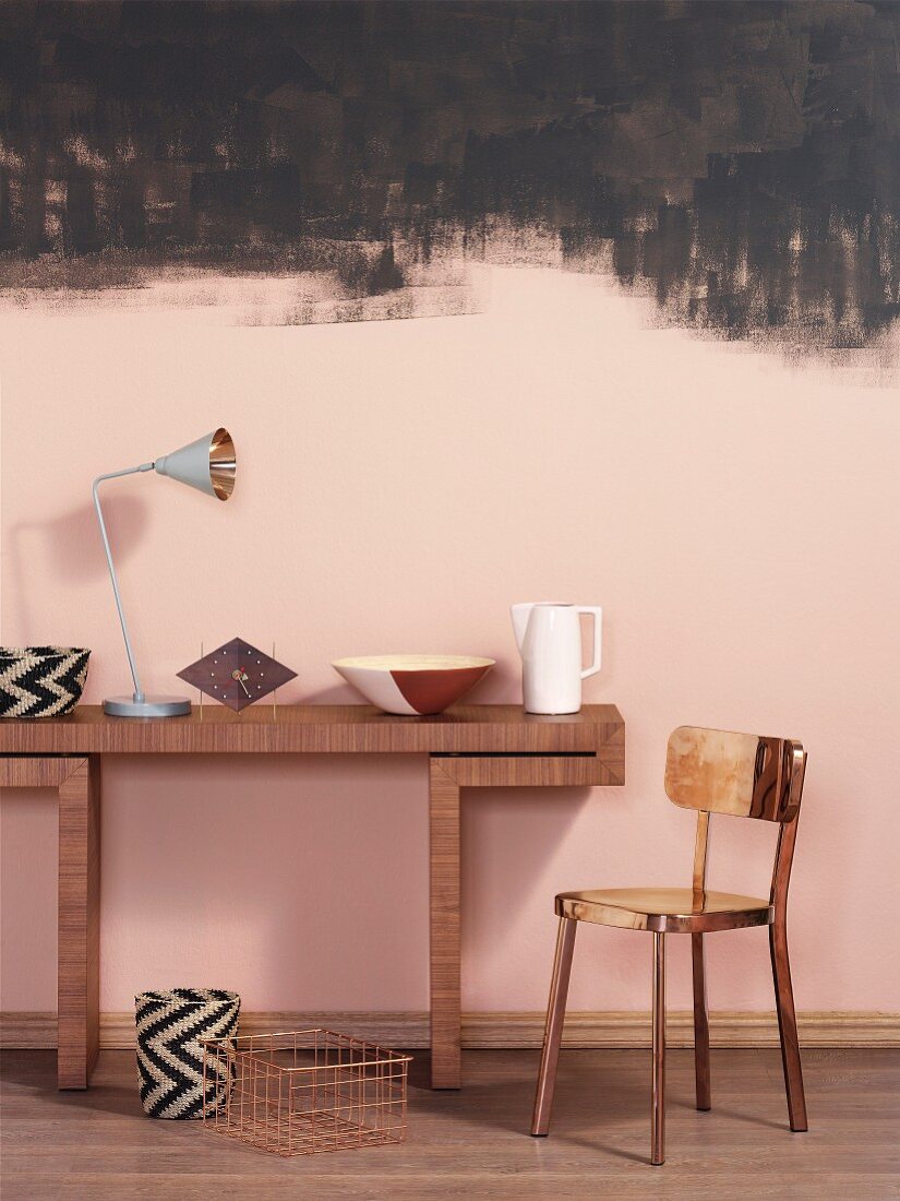 Wandtisch aus Holz mit Dekoobjekten und Metallstuhl vor rosa getönter Wand mit schwarzen Farbspuren