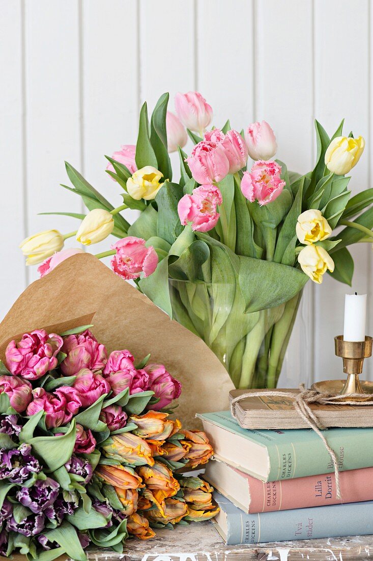 Bouquets of tulips wrapped in paper and in glass vase next to stack of books