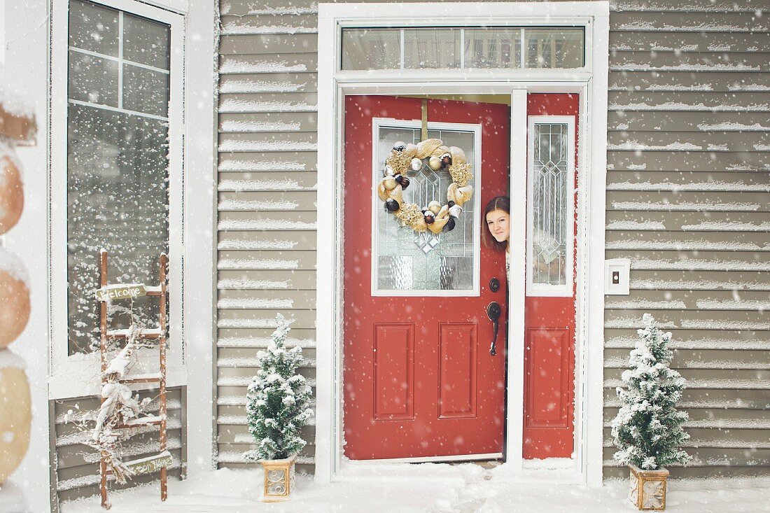 Frau schaut aus geöffneter Haustür in verschneiten Hauseingang