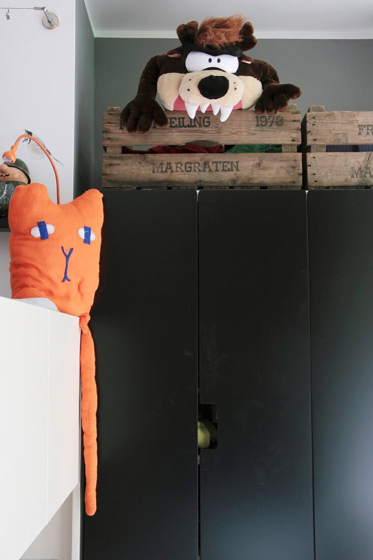 Rustikale Holzkisten mit Stofftier auf schwarzem Schrank, seitlich orangefarbene Tierfigur auf weißem Schrank
