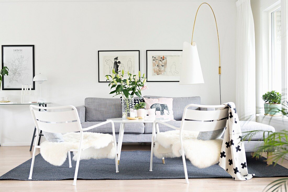 weiße Gartenstühle mit Tierfell, hellgraue Polstercouch und Designer-Stehleuchte im Loungebereich