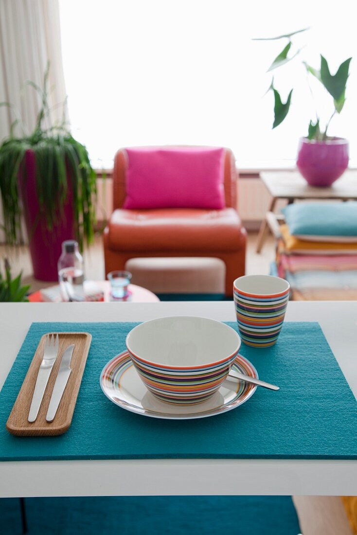Brightly striped crockery on blue felt place mat and view into living room