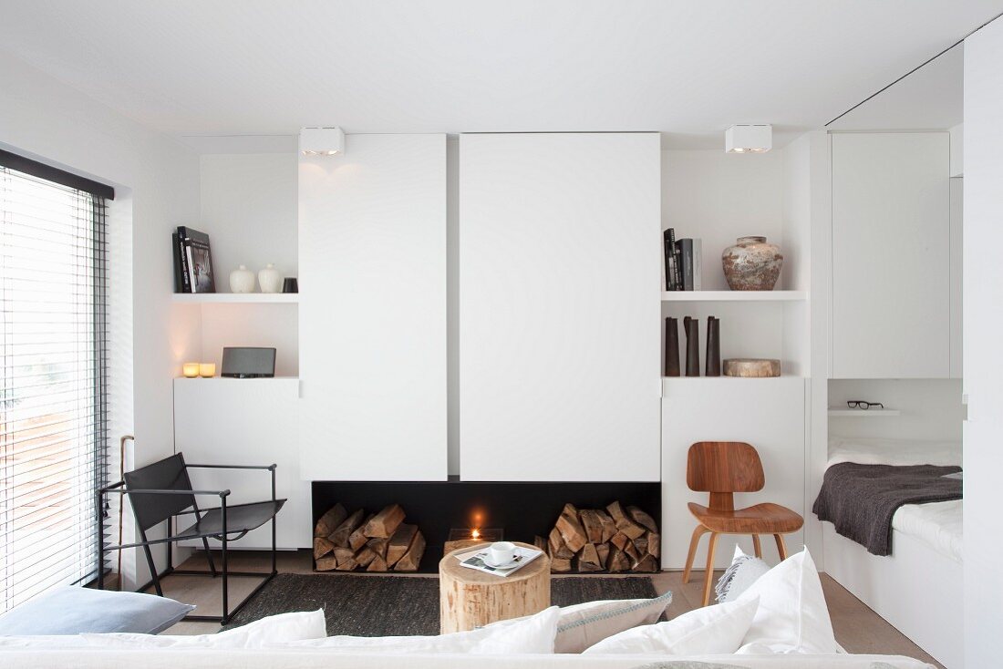 Offener, weisser Wohnraum mit Kamin und Schlafbereich in kleinem Apartment