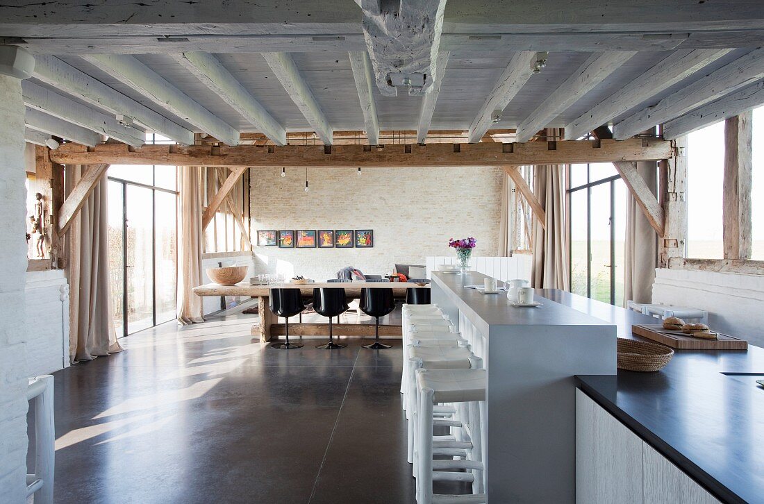 Counter and long dining table in open-plan interior of converted barn with polycrete floor