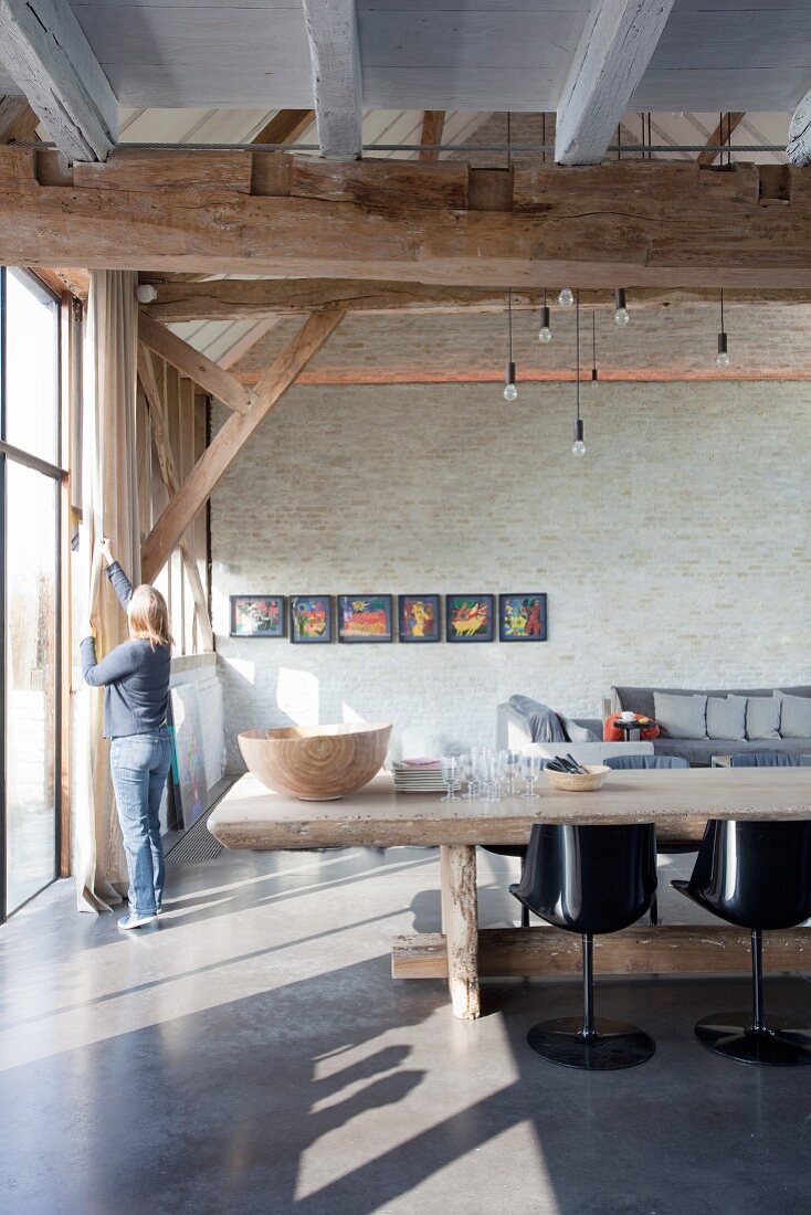 Rustic dining table and designer chairs in converted barn with woman next to window