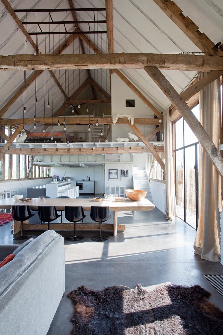 Rustic dining table and designer chairs in converted barn with exposed wood beams and mezzanine level