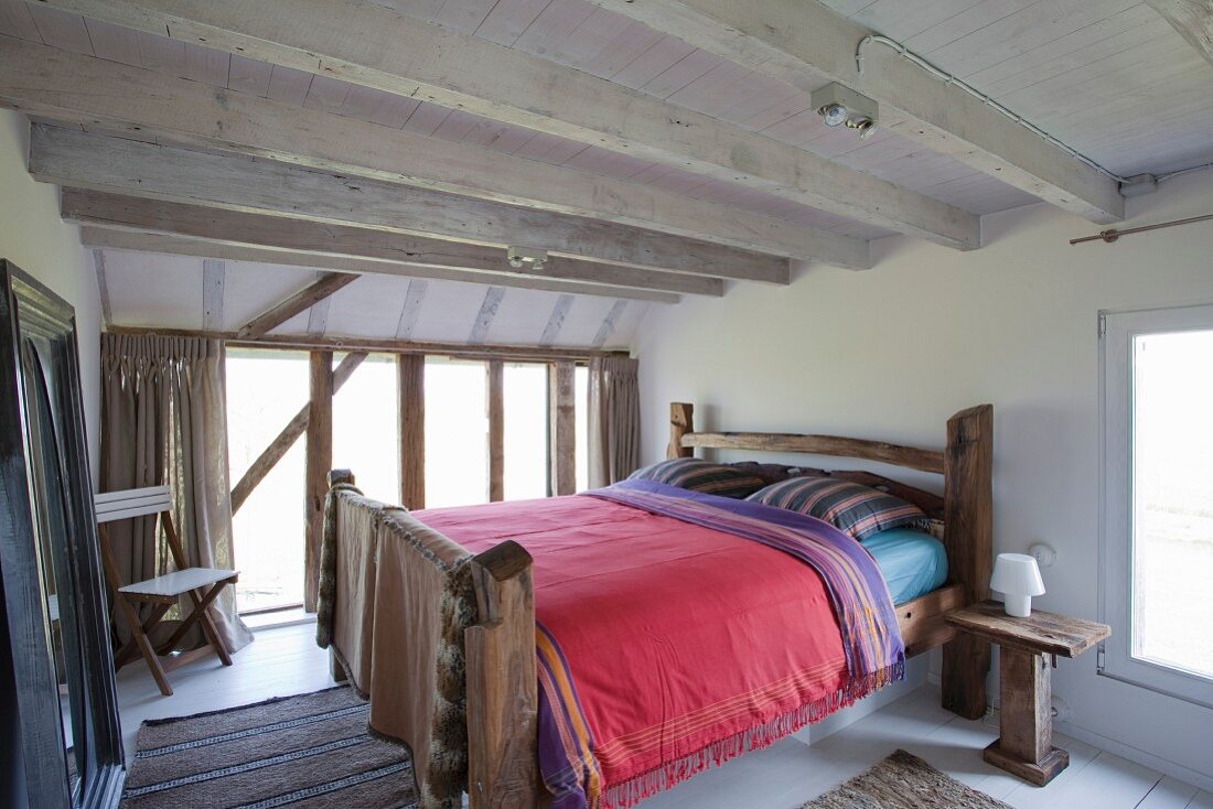 Rustic wooden double bed in bedroom with white wood-beamed ceiling