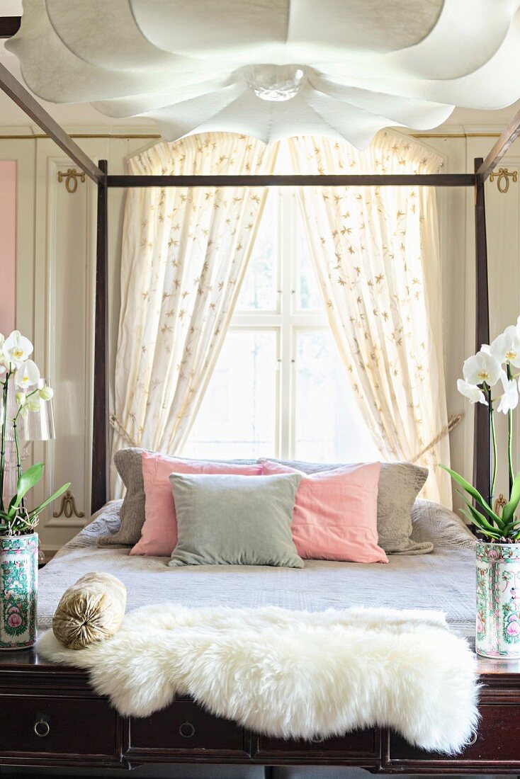 Konsolentisch mit Schaffell und Orchideen, Blick auf Bett mit Holzgestell vor Fenster