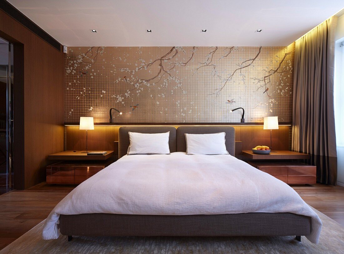 Elegantes Schlafzimmer mit Doppelbett und Polsterkopfteil, dahinter Wandgestaltung mit dekorativen, asiatischen Ästemotiven