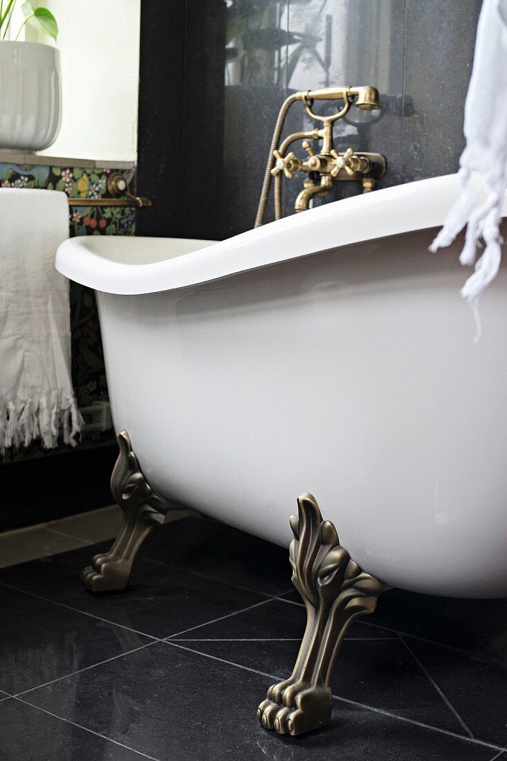Free-standing, vintage bathtub with brass claw feet on black tiled floor