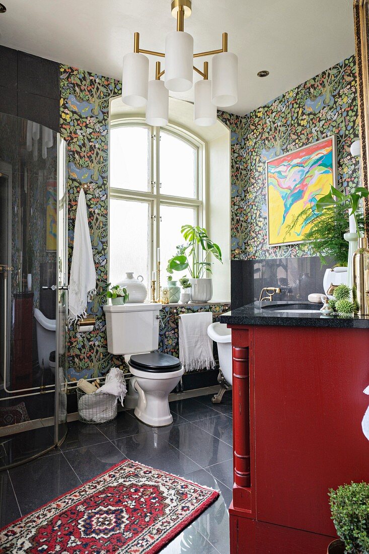 Toilet below window and Oriental rug on black tiled floorr in vintage bathroom