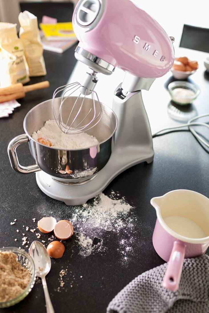 A pink Kitchen Aid working with a stainless steel mixing bowl of ingredients on a black surface