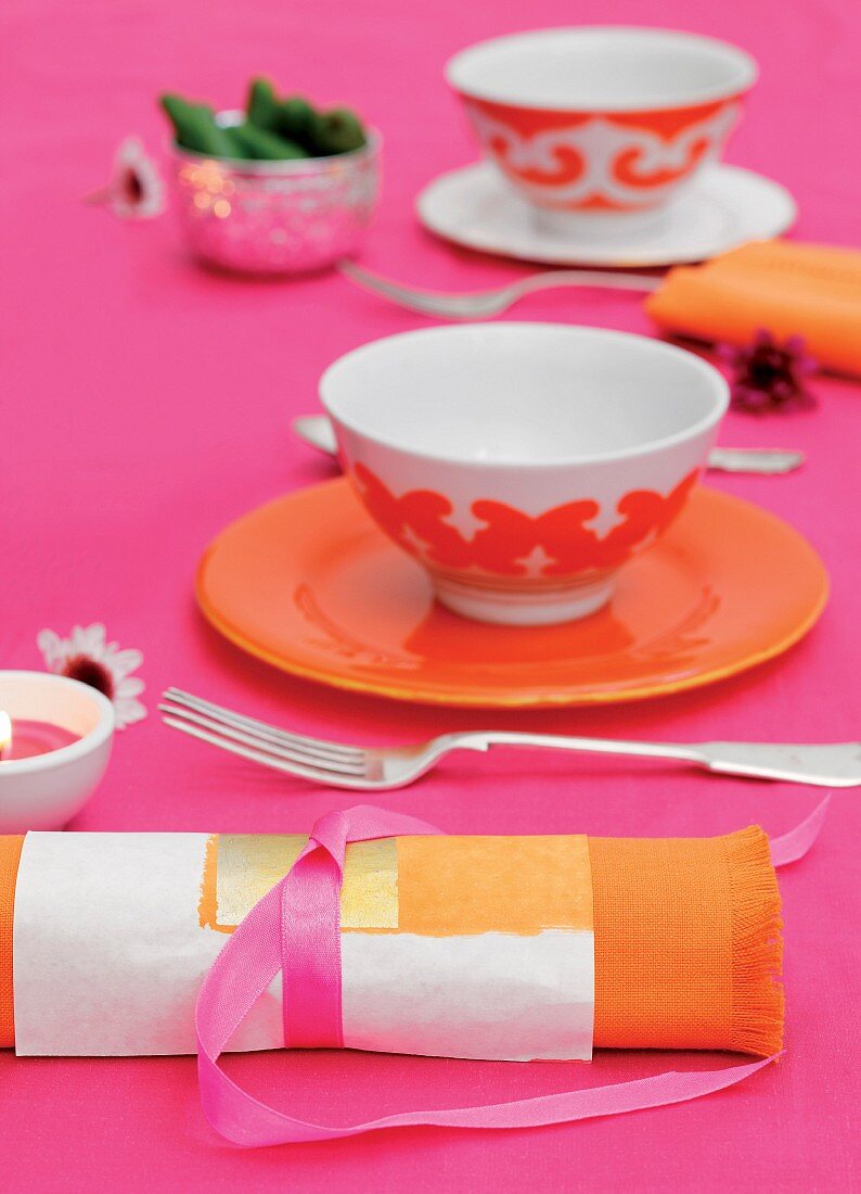 Orangefarbenes Gedeck auf pink Tischdecke und passenede Serviette