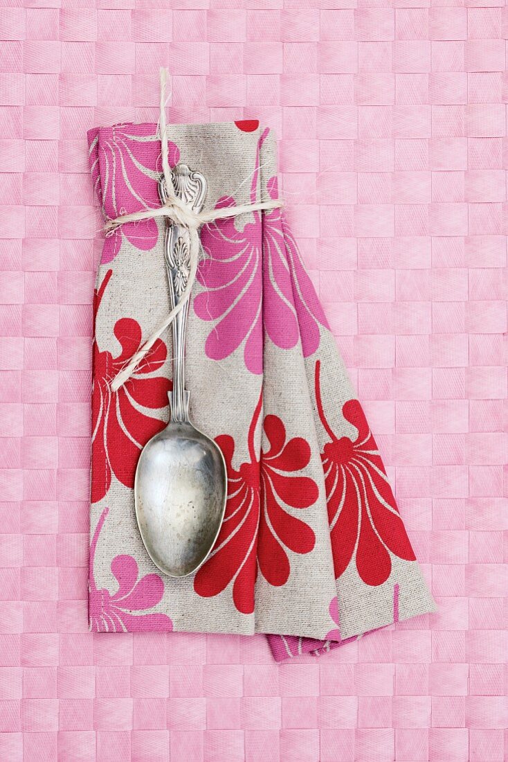 Vintage Löffel auf Leinen Serviette mit Blumenmuster auf rosa Tischset