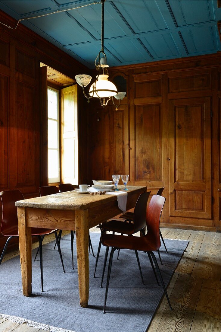Rustikaler Esstisch aus Holz mit Stühlen vor Fenster in holzverkleidetem Esszimmer