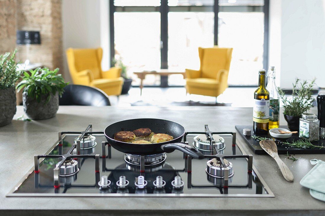 A kitchen island with a concrete work surface and a gas hob with a pt burger in a pan