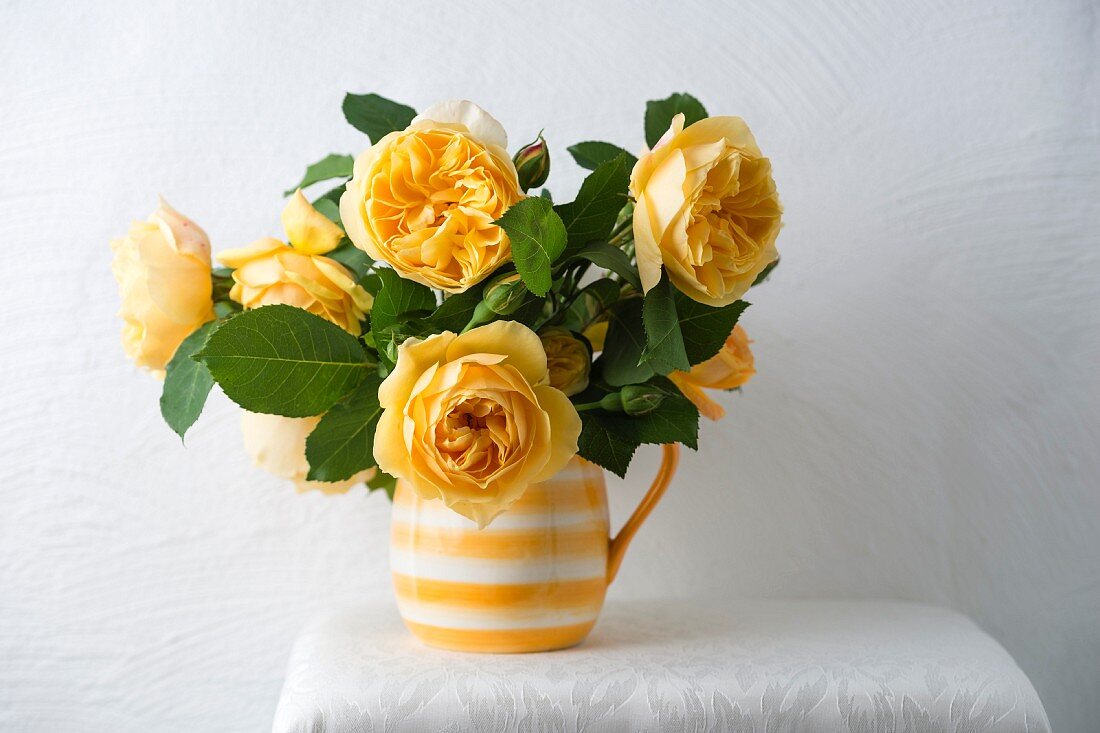 Rosenstrauss aus gelben Rosen in gelb-weiss getreiftem Krug