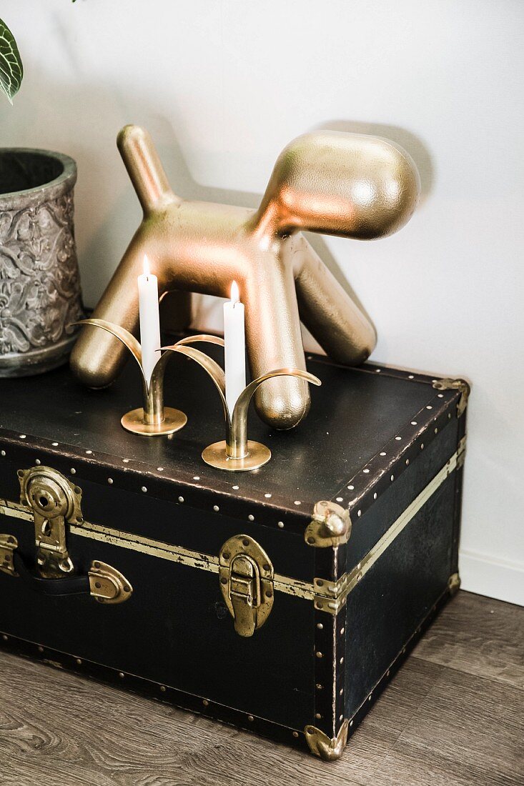 Goldfarbene Hunderfigur und Kerzen auf antikem Mini-Koffer mit Messingverschluss