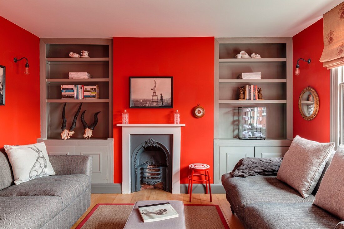 Wohnzimmer mit roten Wänden, grauen Einbauregalen und nostalgischem Kamin