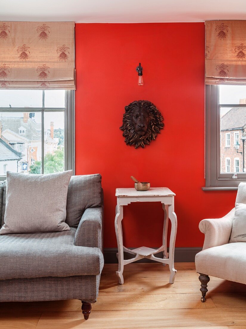 Weißer Vintage Beistelltisch mit Klangschale vor roter Wand und Löwenbüste zwischen Fenstern