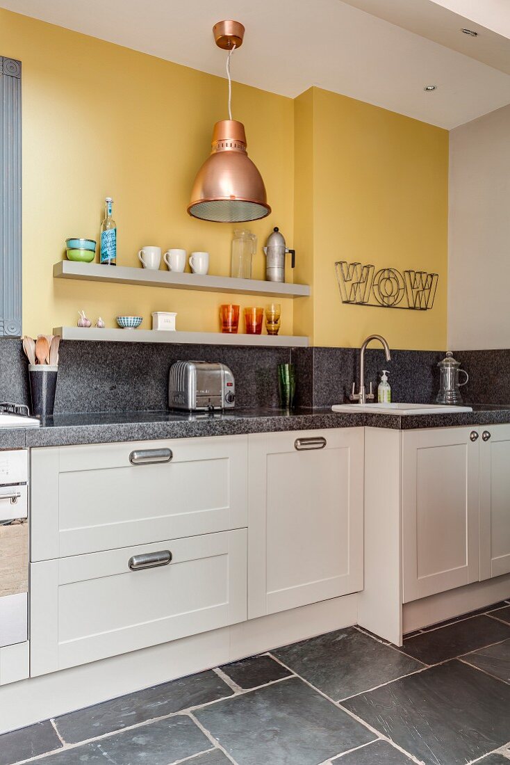 Küchenzeile mit Granit-Arbeitsplatte und zwei graue Wandboards an gelber Wand