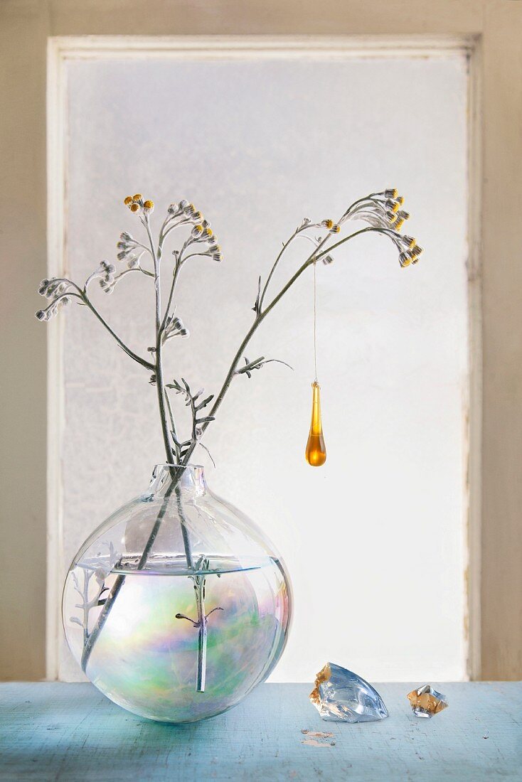 Glass ornament hanging from flowering branch in spherical glass vase