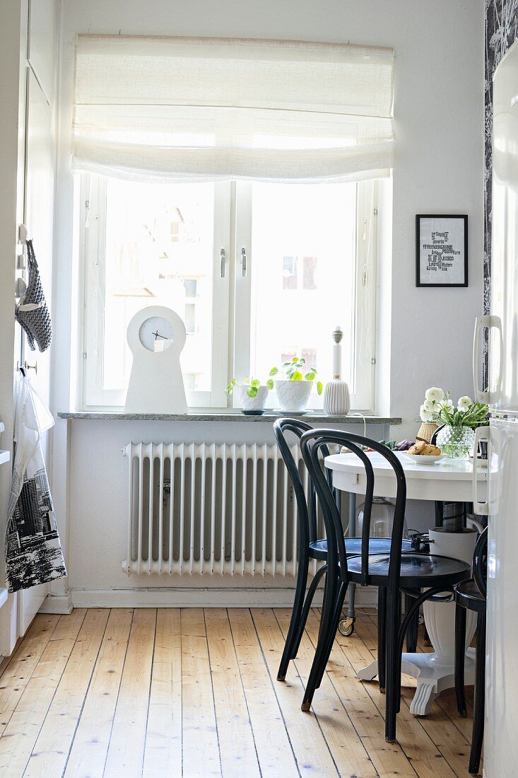 Schwarze Stühle um runden weißen Tisch vor dem Küchenfenster