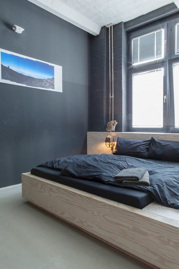 Reduziertes Schlafzimmer mit modernem Holzbett vor schwarzer Wand und Fotografie