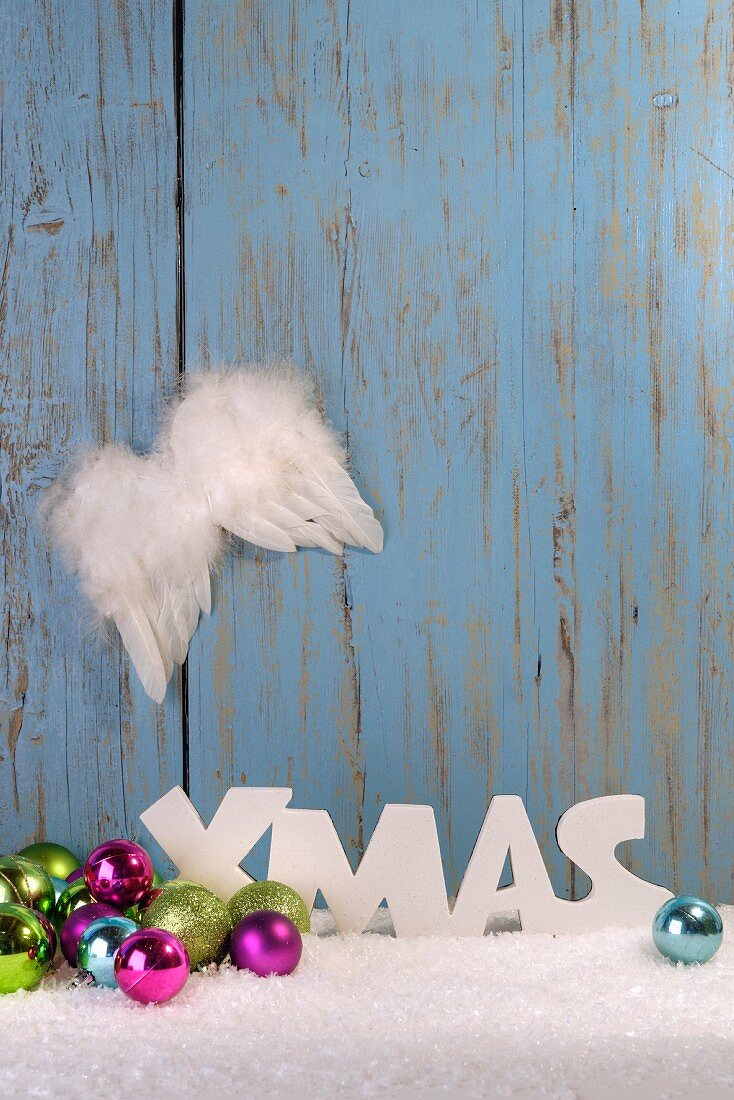 Christmas arrangement of baubles, angel wings and artificial snow in front of wooden wall