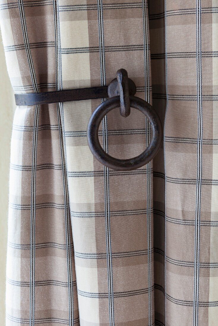 Cast-iron curtain holdback holding checked curtain in shades of beige