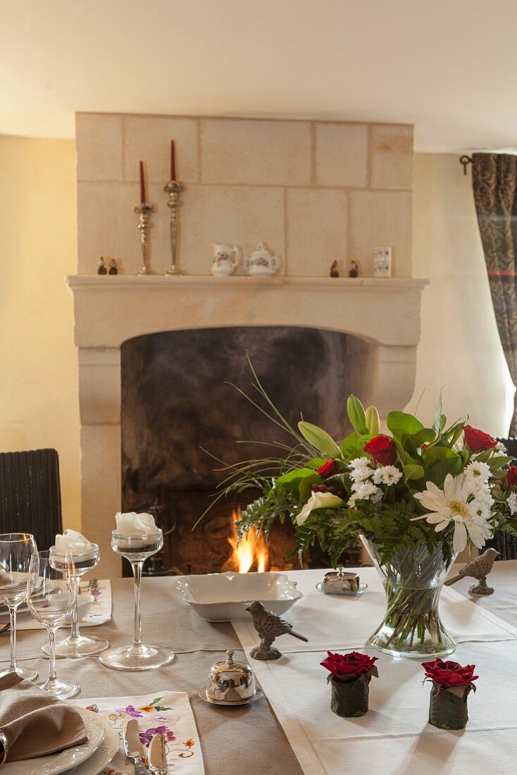 Flower arrangement on festively set dining table and view of open fire